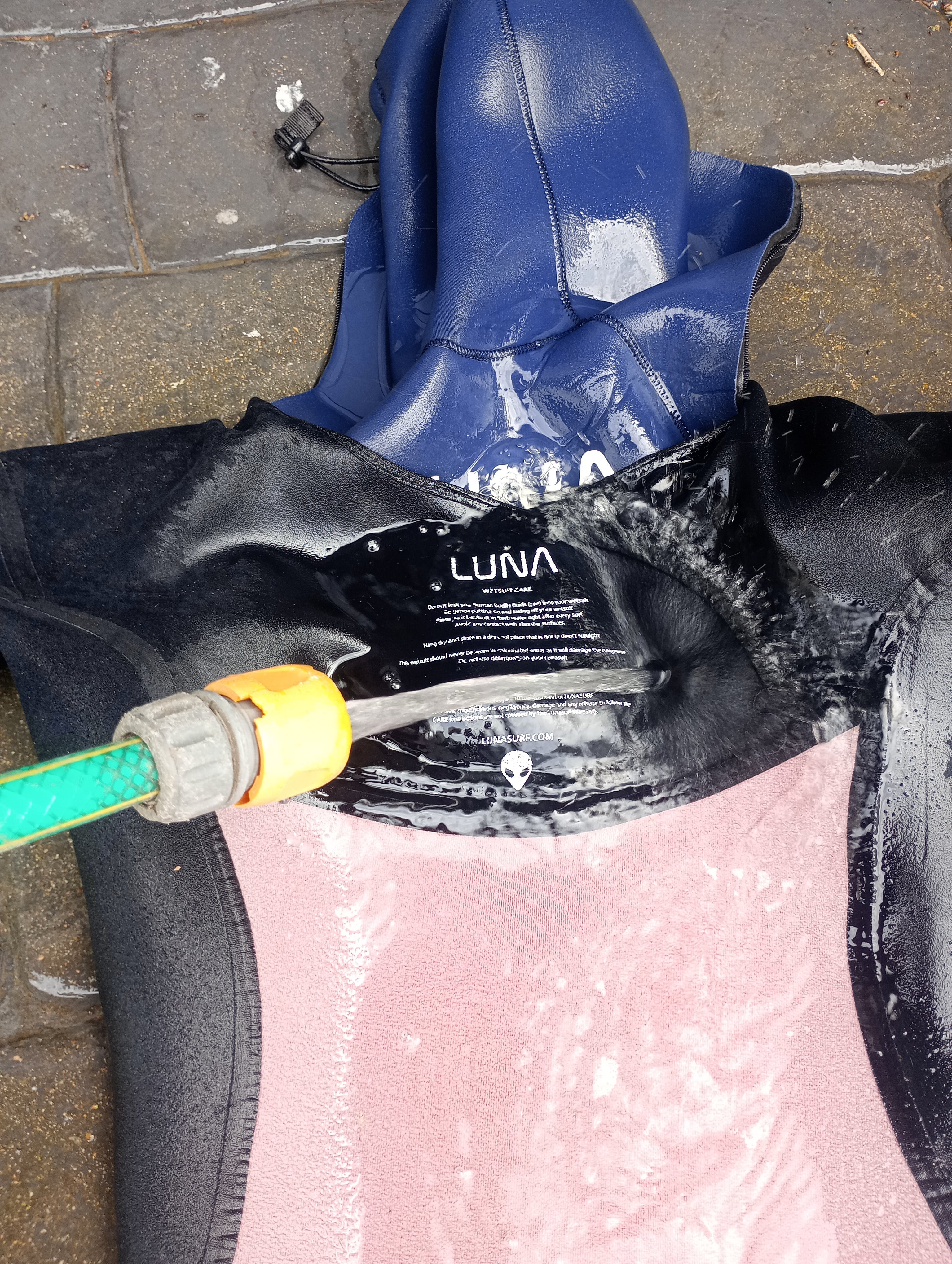 Lunasurf wetsuit hanging on a wide hanger being rinsed with fresh water after a surf session